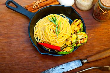 Italian spaghetti pasta with zucchini sauce on iron skillet over wood board