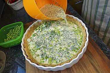 Southern German cuisine, baking, preparing hearty vegetable tart with walnut base, walnut dough in baking tin, dough with green peas, spring onions, filling mass into tart tin, quiche tin, mixing bowl, Germany, Europe