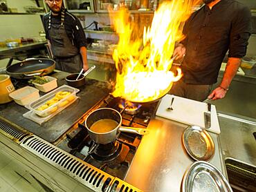 Chef cooking flambleing atlantic squid with olive oil in a big pan in a professional kitchen, trendy seafood recipe, Professional gourmet cooking concept