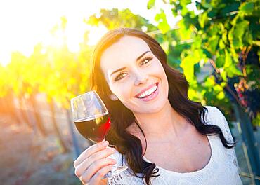 Beautiful young adult woman enjoying glass of wine tasting in the vineyard