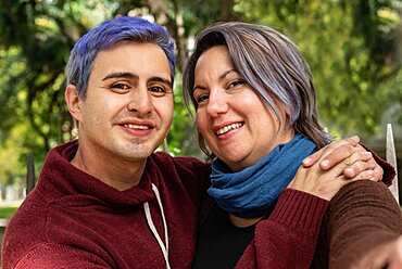 Two smiling friends are hugging and looking at camera. He has blue hair