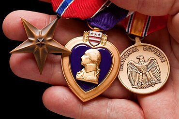 Man holding purple heart, bronze and national defense war medals in the palm of his hand