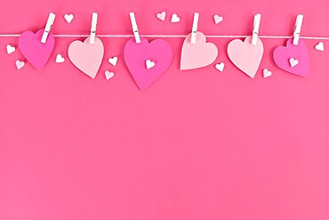 Pink paper hearts hanging from line with pegs and sugar sprinkles