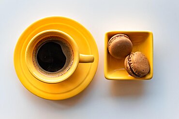 Top angle of a yellow cup of black coffee and two macaroons on white background