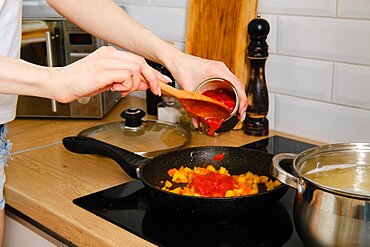 Closeup view of female hand adding canned whole peeled tomatoes into frying pan while preparing pasta sauce