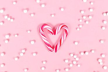 Small striped Christmas candy cane sweets forming heart on pink background