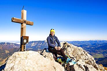 Mountaineer taking a break at the summit cross of the Schaertenspitze, Hochkalter, Berchtesgaden Alps, Berchtesgaden National Park, Ramsau, Berchtesgadener Land, Upper Bavaria, Bavaria, Germany, Europe