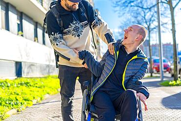 Disabled person in a wheelchair laughing with a friend in a chair on the street in winter