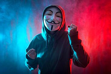 Hacker with anonymous mask with a symbol of fight, with a background of smoke and colored led