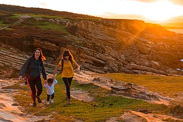 Two sisters with a child watching the sunset on the coast by the sea, family lifestyle