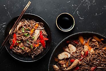 Bowl with Asian chicken stir fry soba noodles with vegetables on dark black stone background from above, Chinese Thai or Japanese noodles dish with soy sauce