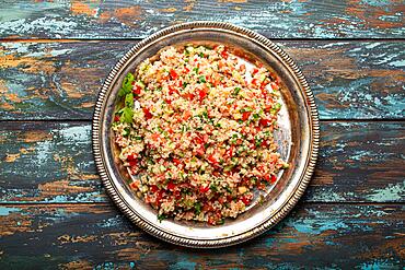 Middle eastern and Mediterranean traditional vegetable salad tabbouleh with couscous on rustic metal plate and wooden background from above. Arab Turkish food