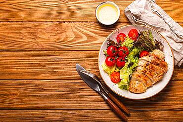 Healthy green vegetable salad with grilled chicken breast fillet on ceramic plate on rustic wooden kitchen table top view flat lay, diet food and clean eating concept, space for text background