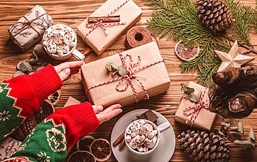 Christmas flat lay with female hands tying a ribbon on a present, gift boxes, fir tree branch at wooden background. Wrapping Xmas present top view, cozy festive composition