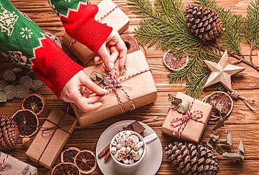 Christmas flat lay with female hands tying a ribbon on a present, gift boxes, fir tree branch at wooden background. Wrapping Xmas present top view, cozy festive composition