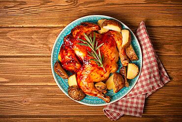 Delicious roasted whole chicken with glazed gold crispy skin on big ceramic plate top view on wooden rustic background top view, traditional tasty dinner