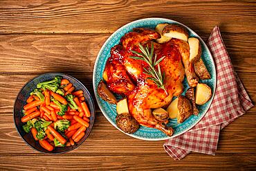 Delicious roasted whole chicken and vegetables in bowl top view on wooden rustic background top view, traditional tasty dinner