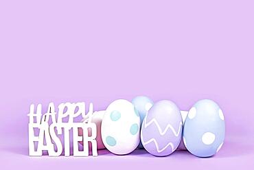 Pastel colored easter eggs and text Happy Easter on violet background with copy space