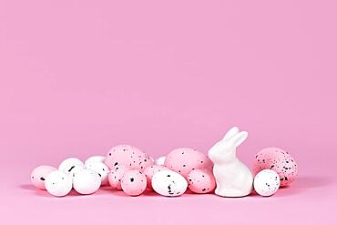 White and pink Easter eggs with small bunny sculpture on pink background with copy space