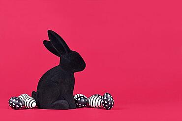 Black and white easter eggs with hearts and stripes next to bunny figure on pink background