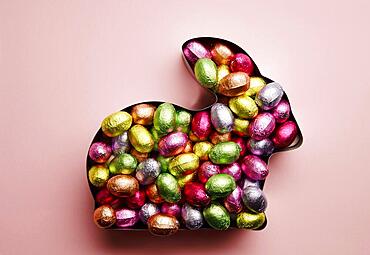 Easter bunny in baking tin filled with chocolate eggs on a salmon background