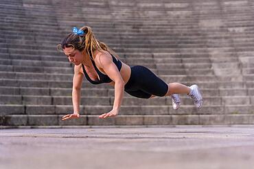 Caucasian young woman doing fitness in a city park, doing a push-up and acrobatic jump on the mat