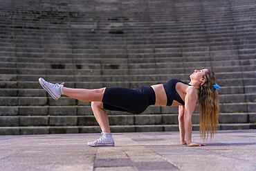 Caucasian young woman doing fitness in a city park, squats to work legs and buttocks