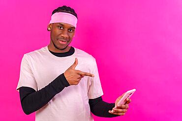 Black ethnic man with a phone in pink clothes on a pink background, talking on the phone