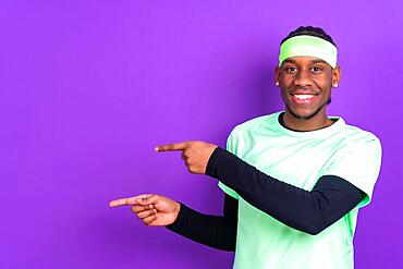 Black ethnic man in green clothes on a purple background, pointing at a free copy space