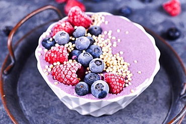 Fruit smoothie bowl with yogurt decorated with healthy raspberry, blueberry and puffed quinoa grain on iron tray