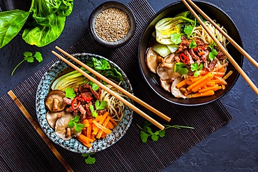 Asia style ramen soup with udon noodle, beef, shiitake, pak choi cabbage and carrots on black background