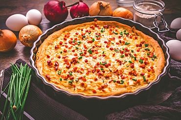 Homemade onion tart or pie with bacon and chives on wooden background