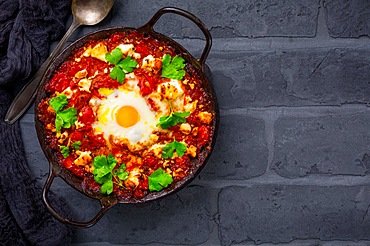 Shakshouka - dish of eggs poached in a sauce of tomatoes, olive oil, peppers, onion and garlic on black background