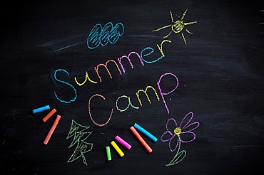 Text Summer camp written on black chalkboard, with chalk sticks of different colors