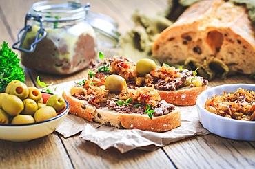 Fresh homemade chicken liver pate on ciabatta bread with roasted onions and olives on wooden table