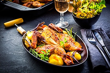 Baked whole chicken with potatoes, carrots, herbs and salt and rose wine on black background