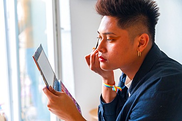 A man is applying makeup and looking at a tablet