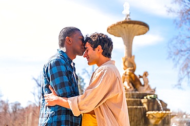 Couple of multi-ethnic men in a city fountain, lgbt concept, in a romantic pose kissing each other on the forehead