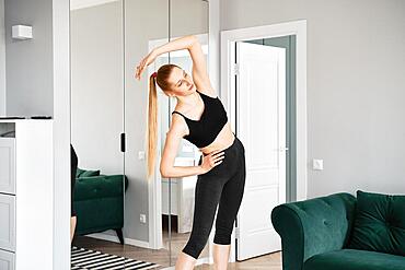 Active blonde woman does bending exercises in bright apartment