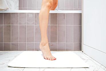 Unrecognizable young woman is stepping over edge of bathtub on a towel thrown on the floor after taking bath