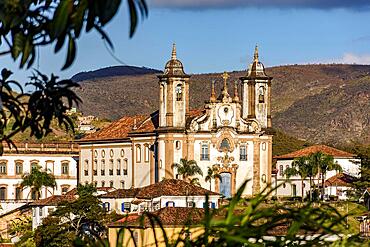 One of the main historic churches in the city of Ouro Preto seen through the vegetation with the mountains in the background, Brasil