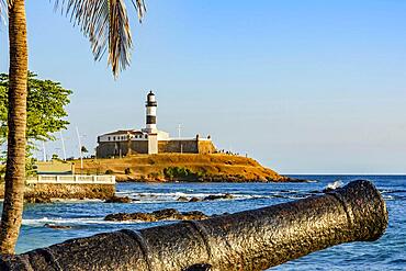 Old cannon and the Barra Lighthouse (Farol da Barra) one of the main historical buildings and tourist spot in the city of Salvador in Bahia surrounded by the sea during the late afternoon., Brasil