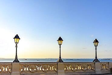 Old colonial style lanterns lighting on walls in the streets of Salvador with the All Saints bay in the background with their boats during the sunset, Brasil