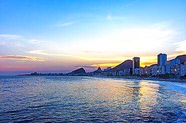 Copacabana beach sunset in Rio de Janeiro with the light coming from behind the buildings and hills, Brasil