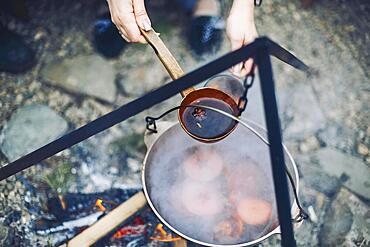 From above traditional mulled wine with slices of orange preparing in pot over burning logs in winter in countryside