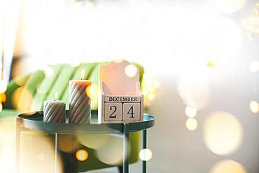 Christmas eve date. December 24 on wooden calendar standing on small table with burning candles in living room, selective focus. Christmas and New Year concept