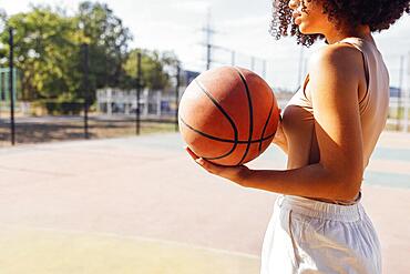 Mixed-race young smiling female outdoors and having fun. Stylish cool teen girl gathering at basketball court, playing basketball outdoors