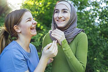 Strong female friendship. Happy two teen girls best friends holding hands and hugging while standing in front of park. Multiethnical friends