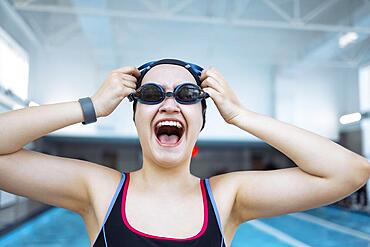 Portrait of a fit woman catcher in the pool looking to the camera. Portrait of a competitive female catcher near the use. Young swimmer wears a swim cap and puts away goggles