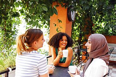 Multiethnic group of girls wearing casual clothes and traditional hijab bonding and having fun outdoors. Three young teen girls in garden cafe drinking tea or coffee